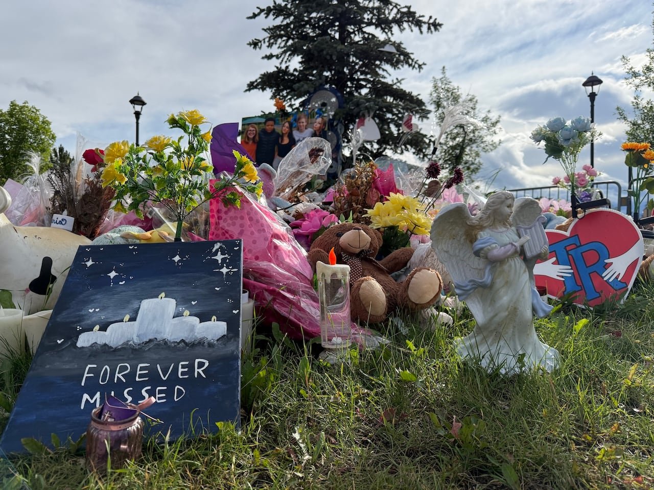 An outdoor memorial in front of a spruce tree with various tributes for the victims of the mass shooting at Tumbler Ridge Secondary School.