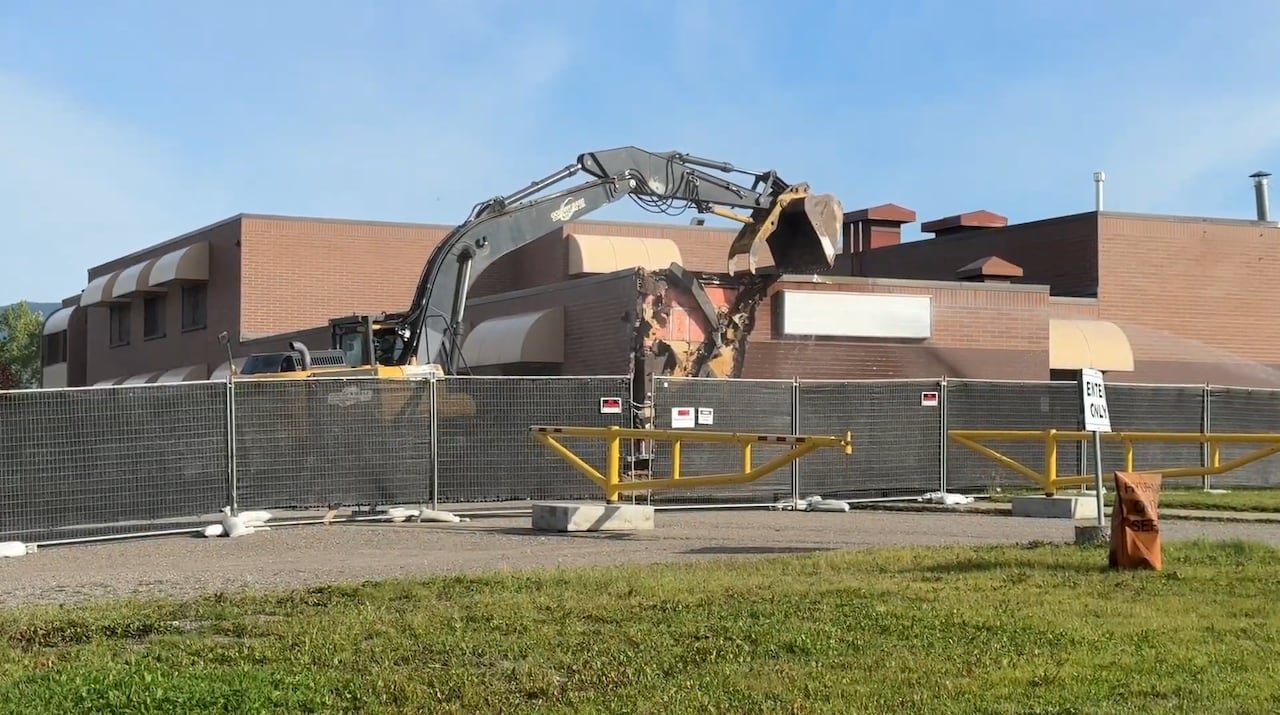 An excavator demolishing a section of the school building, exposing its brickwork.